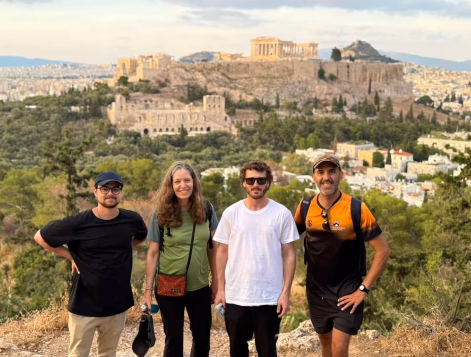 Happy tour group with their Athens tour leader George in the orange Ultimate Athens shirt, the Acropolis behind them